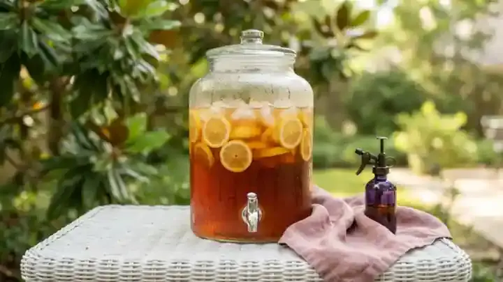 A white wicker porch table with a glass dispenser of iced tea with lemon slices, condensation running down the glass